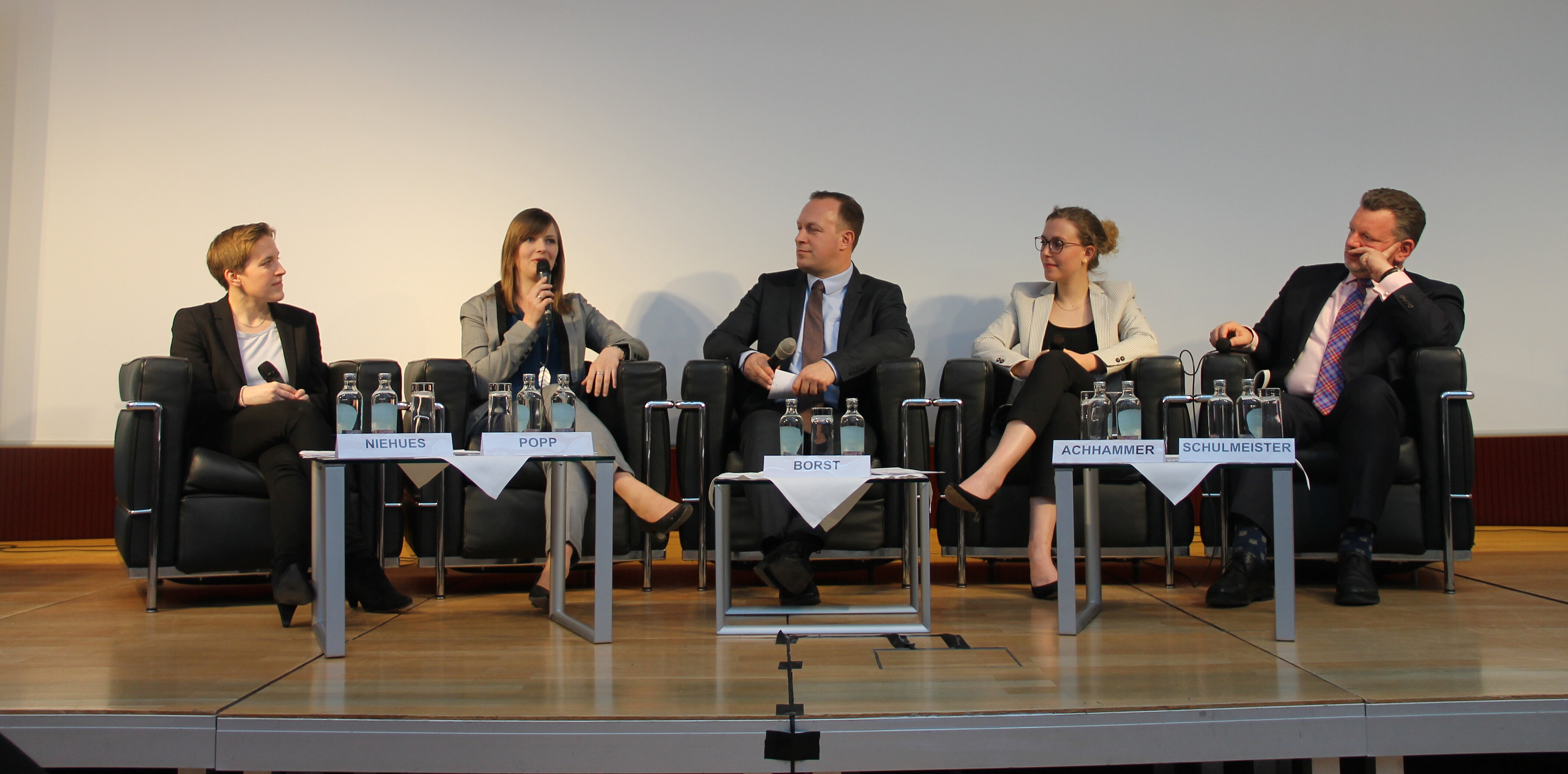 Fünf Personen sitzen auf einer Bühne, während Annika Popp mit Mikrofon leidenschaftlich spricht und die anderen aufmerksam zuhören.