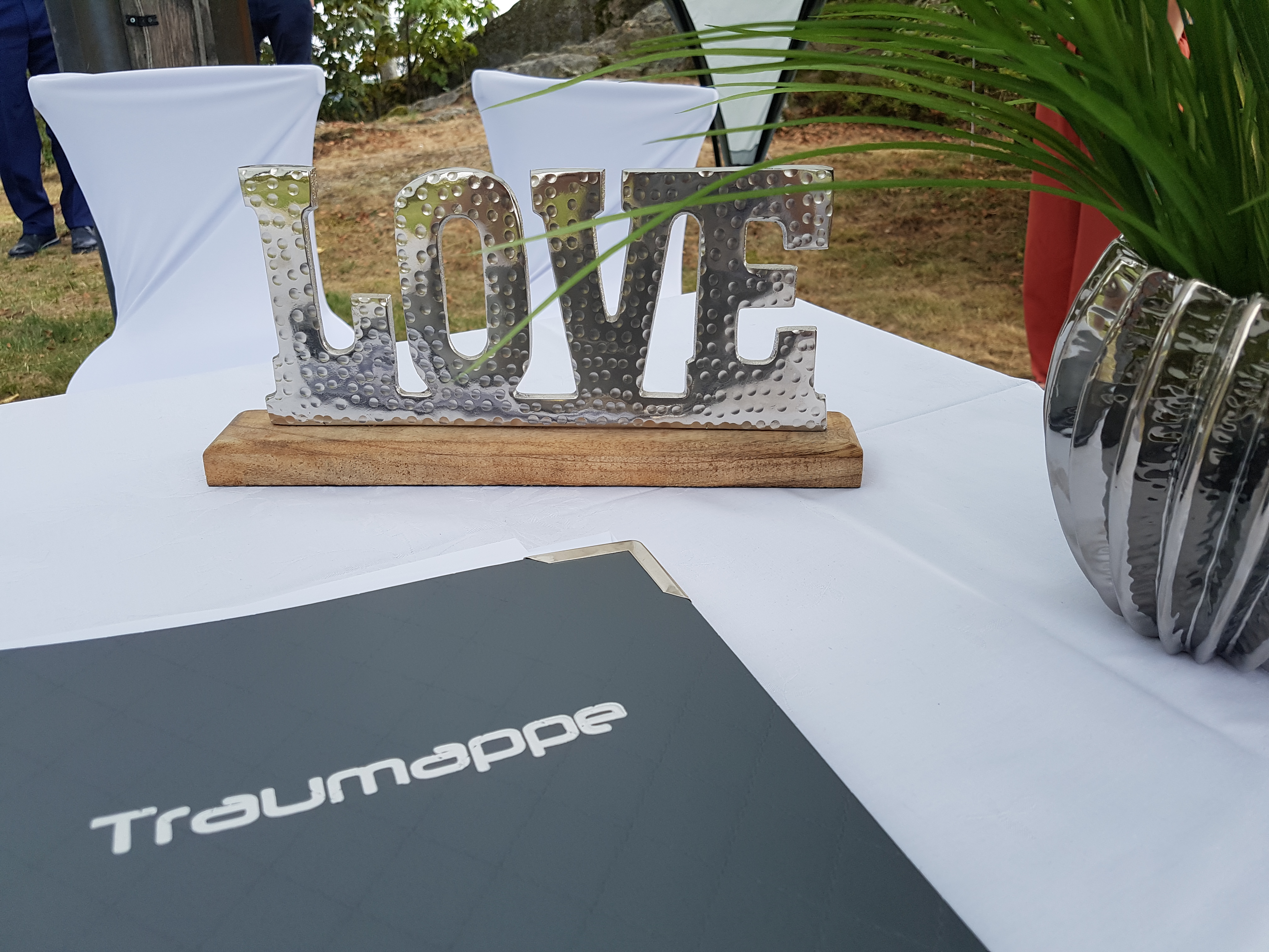Auf einem festlich gedeckten Tisch liegt eine Traummappe, während eine glänzende 'LOVE'-Dekoration im Vordergrund steht.
