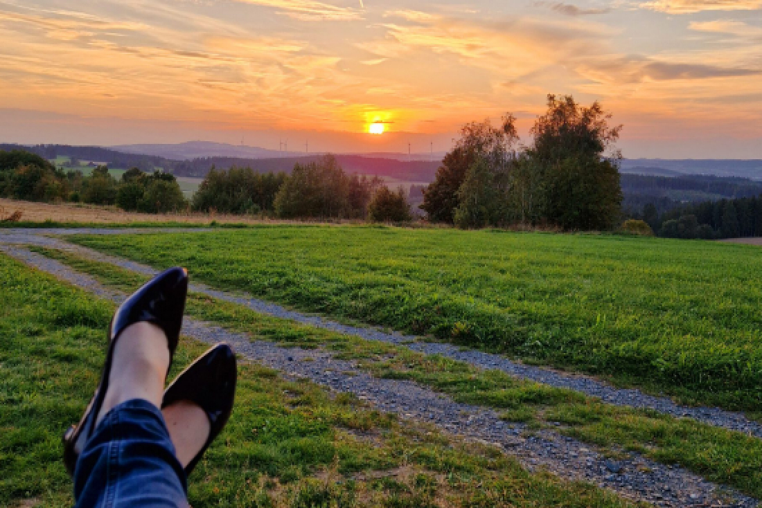 Ein entspannter Blick auf einen Sonnenuntergang über einer grünen Wiese, während jemand die Füße hochlegt.